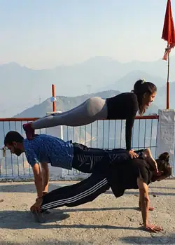 Two students in a partner plank balance on a hilltop with mountain views