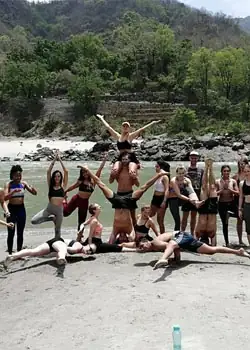 Students in a group pose on the riverbank at the foot of forested hills